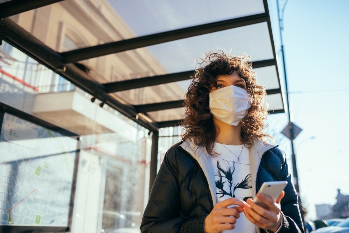 young woman wearing medical face mask standing at public transport stop