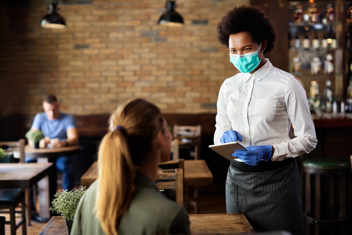 waitress wearing protective face mask while taking order from customer on a touchpad in a cafe.