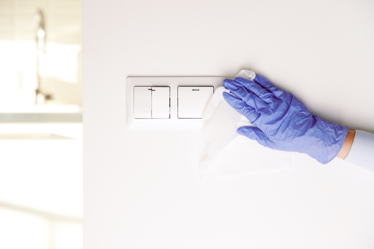 female hands in blue latex gloves, cleaning light switches with towel