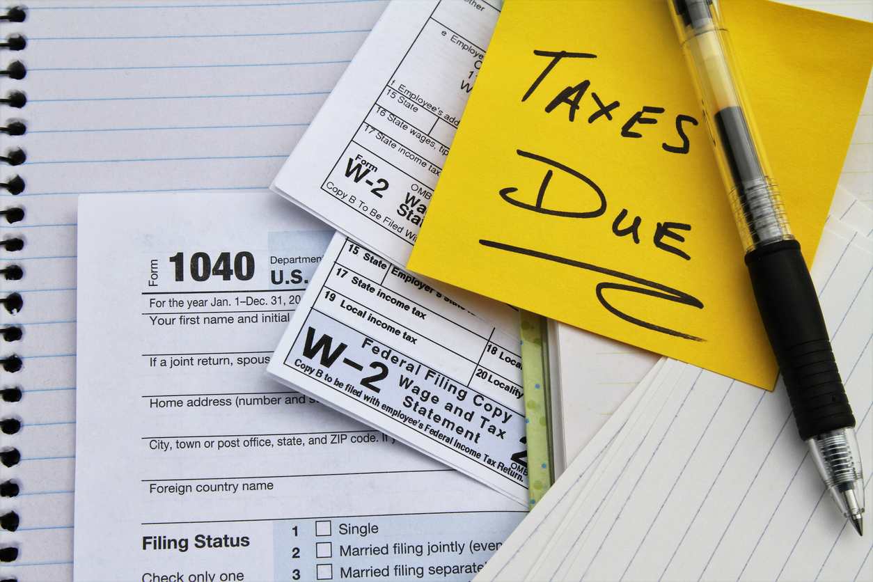 A close up of tax forms with a note on a yellow post-it that says 