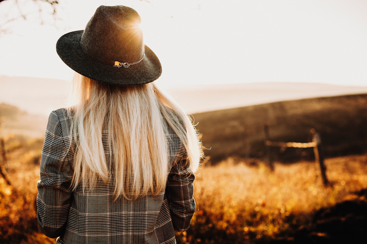 Back view of a lovely blonde girl dressed jacket and hat and looking at epic view at the sunset.
