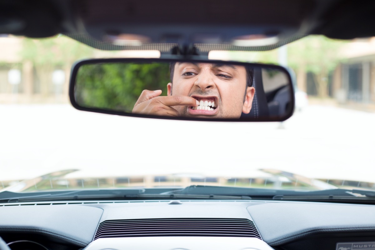 man driver looking at rear view mirror to pick teeth with finger