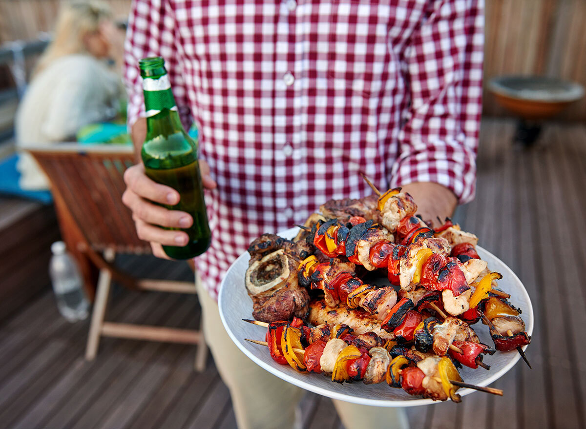 man holding plate of grilled food with beer