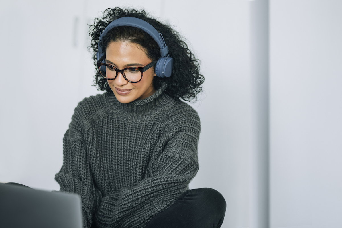 Woman working on her laptop with large headphones, wearing a dark gray sweater