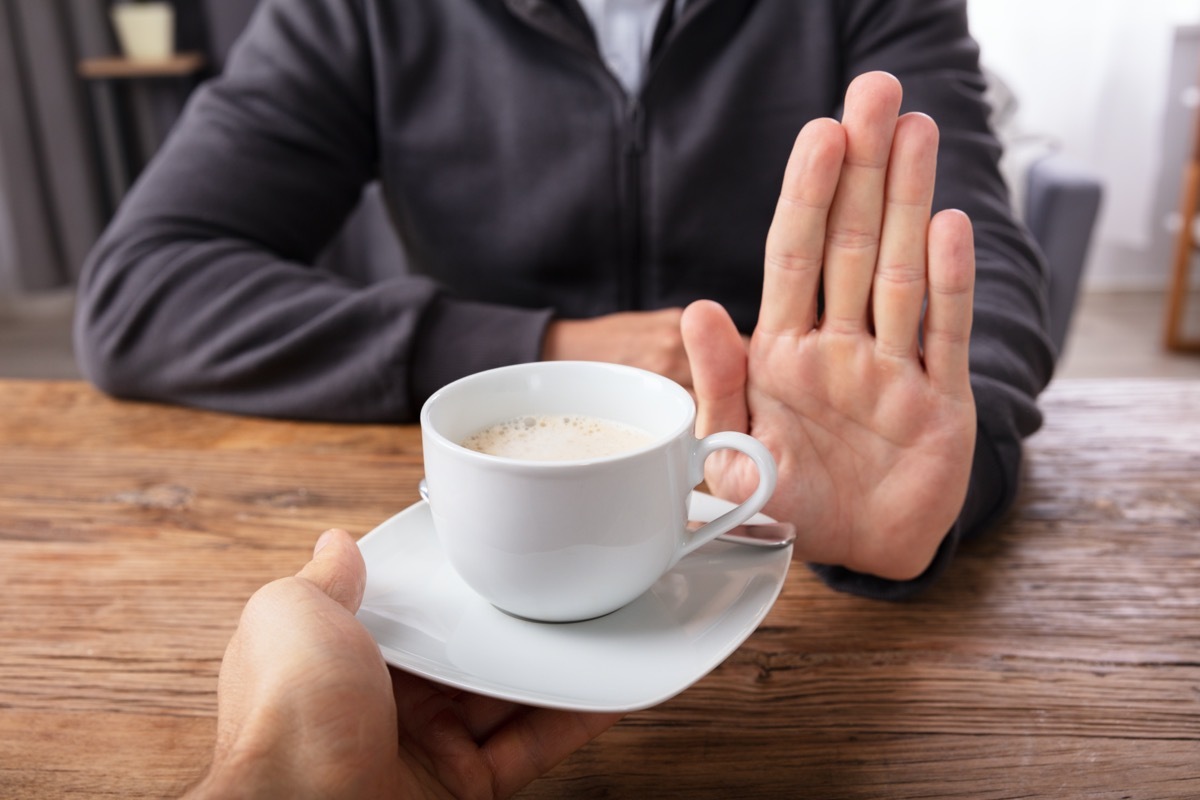 Close-up Of A Man's Hand Refusing Cup Of Coffee Offered By Person Over Wooden Desk