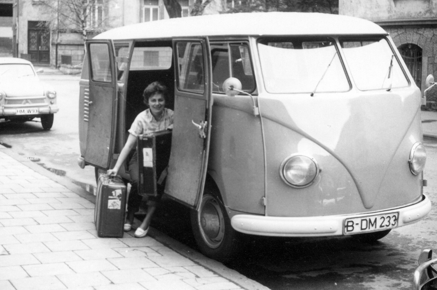 a woman sits in a camper van with two suitcases