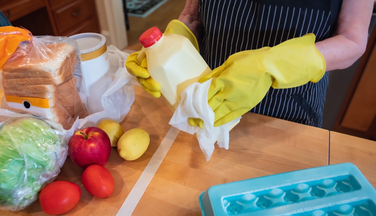 Woman wearing gloves and using disinfectant sanitizing wipes to clean grocery items to prevent the spread of the COVID-19 virus