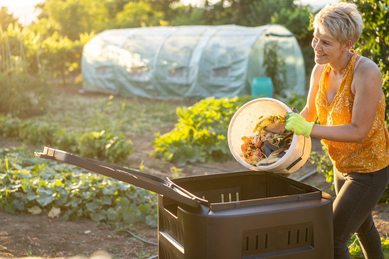 A woman putting food scraps into a compost bin in her garden