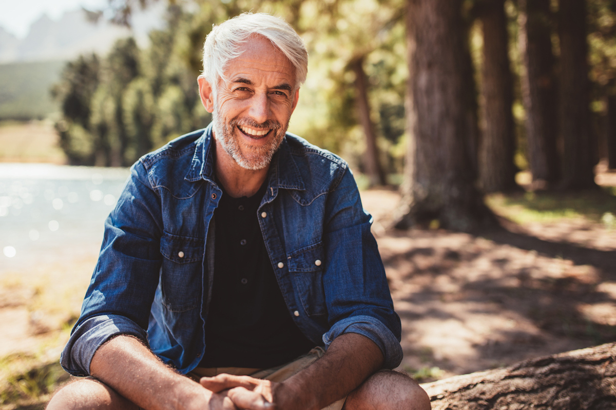 happy mature man sitting near a lake looking at camera and smiling