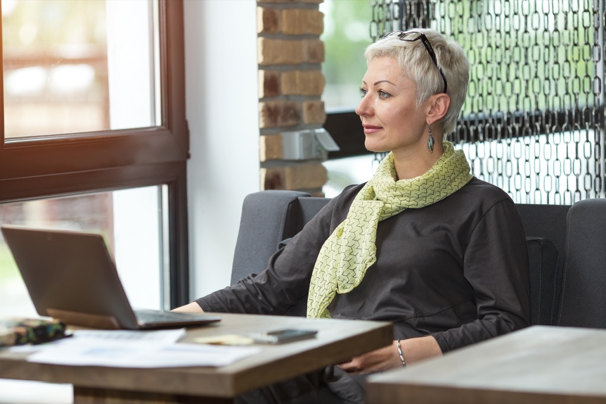 Woman doing work on laptop sitting in deep thought looking out the window