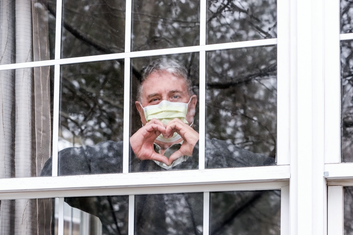 Senior man wearing mask and standing in window