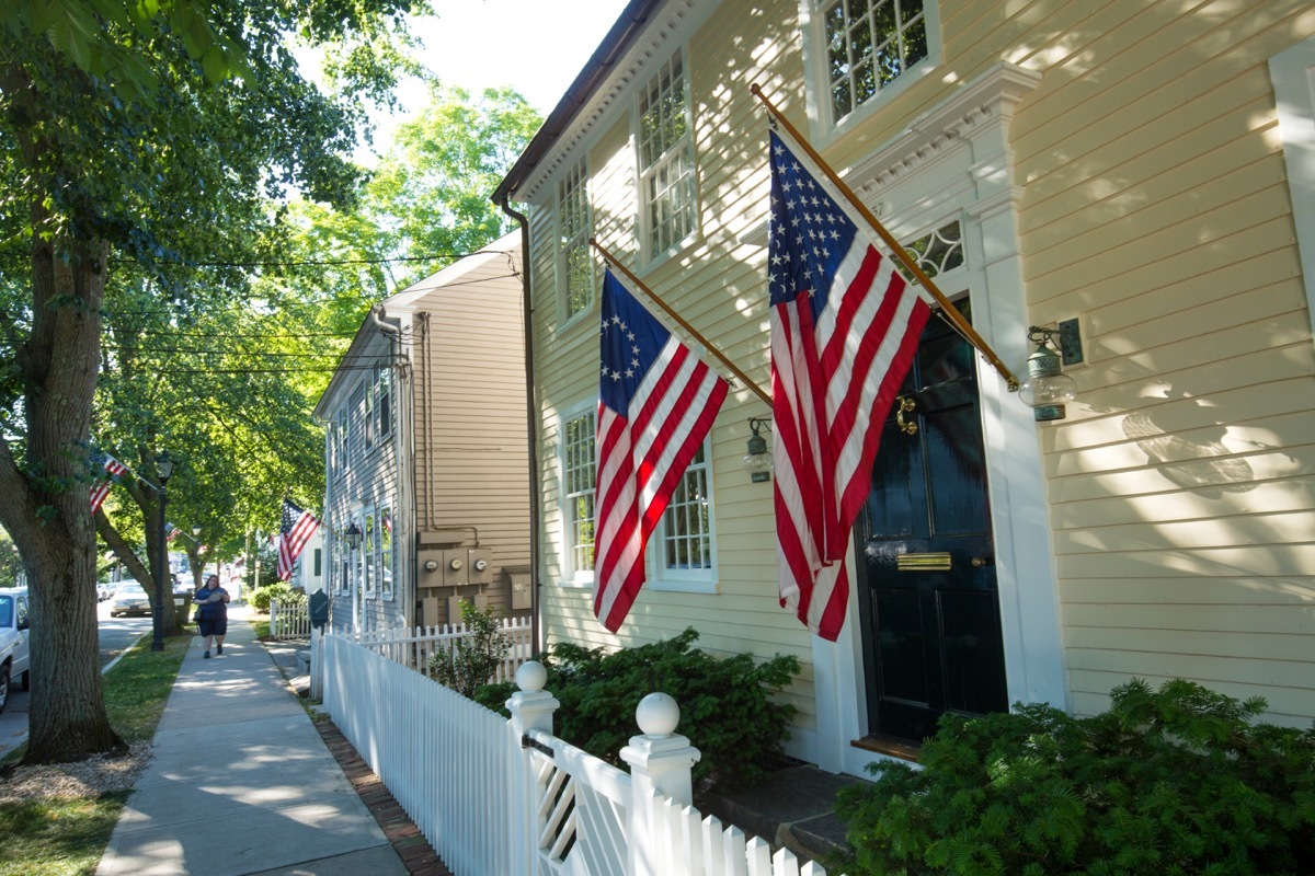 ESSEX, CONNECTICUT, USA - June 19, 2018: American flags and a white picket fence line Main Street in Essex, an all-American village. - Image