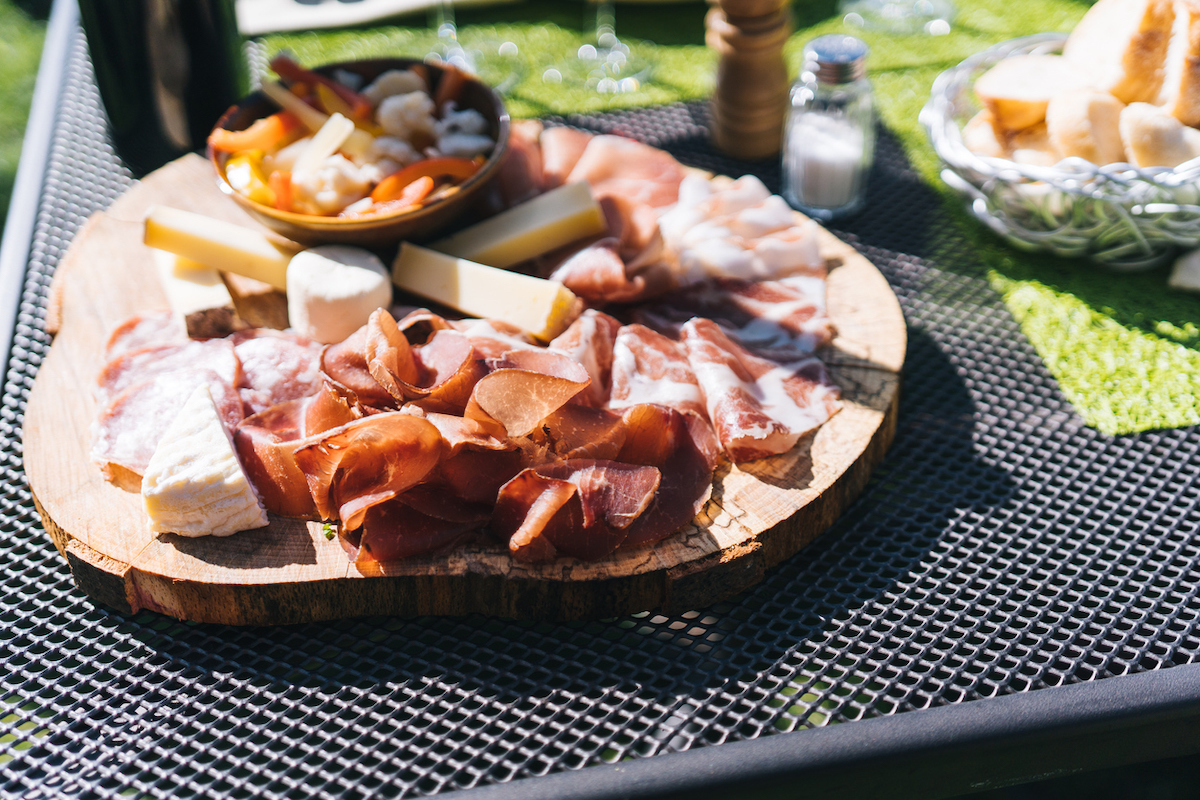 View of charcuterie board in the sunshine containing cheese and Italian meats