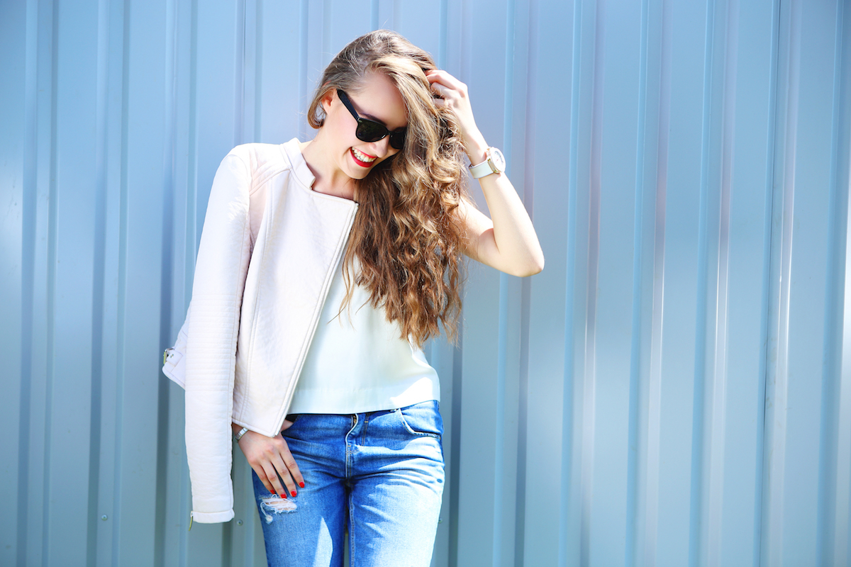 fashion model with long curly hair wearing sunglasses posing outdoor. Jeans, leather jacket.