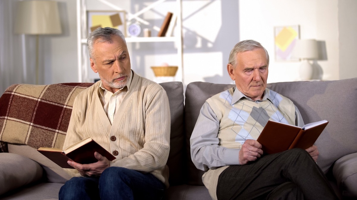 Two offended male friends reading books on sofa at home