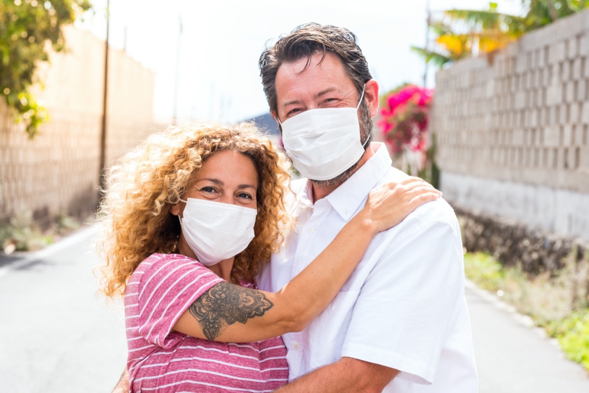 couple of happy people in love smiling and looking at the camera wearing medical and surgical mask on the face to prevent covid-19 or any type of disease or flu
