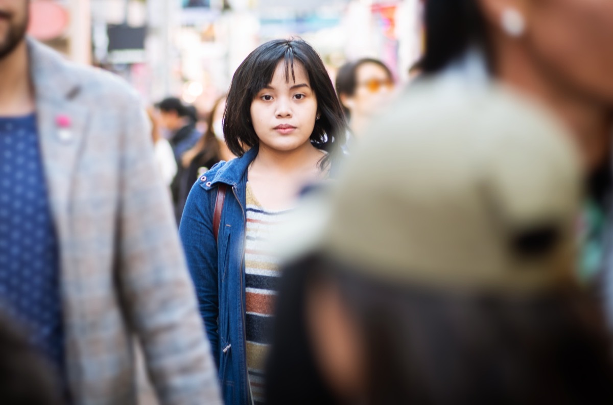 A young woman standing in the middle of a crowded street, looking at the camera.