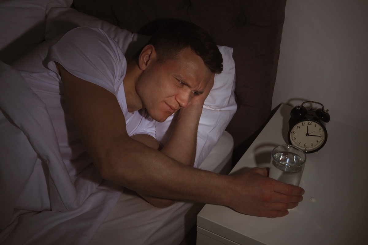 30-something white man reaching for glass of water in bed