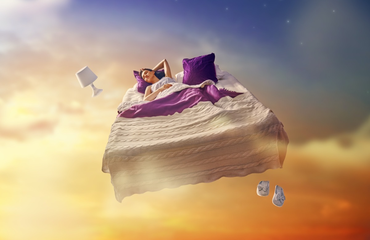 Sleeping woman in bed floating through a starry sky
