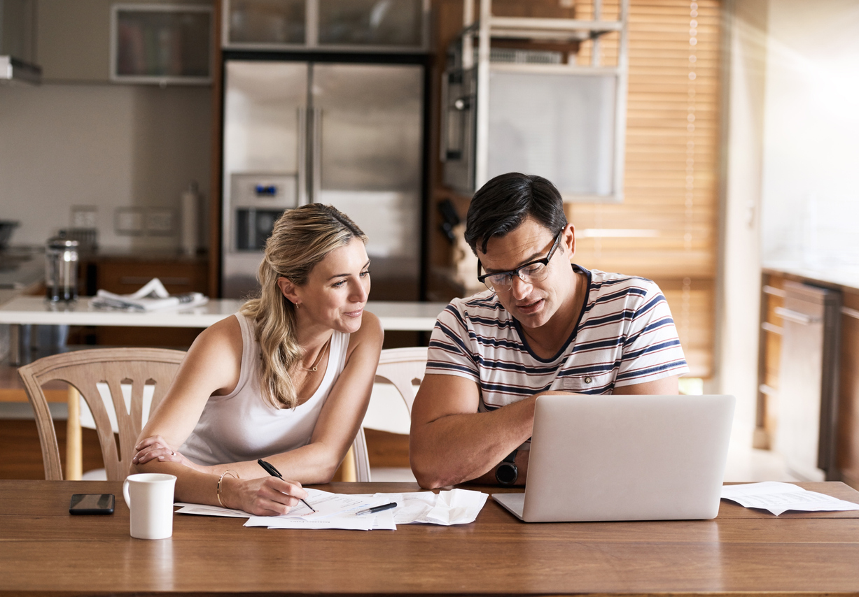 A couple sitting at their kitchen table going over their budget or taxes with a laptop and papers