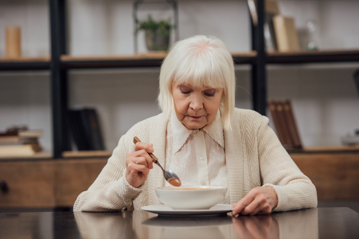 sad lonely senior woman sitting at table and eating at home
