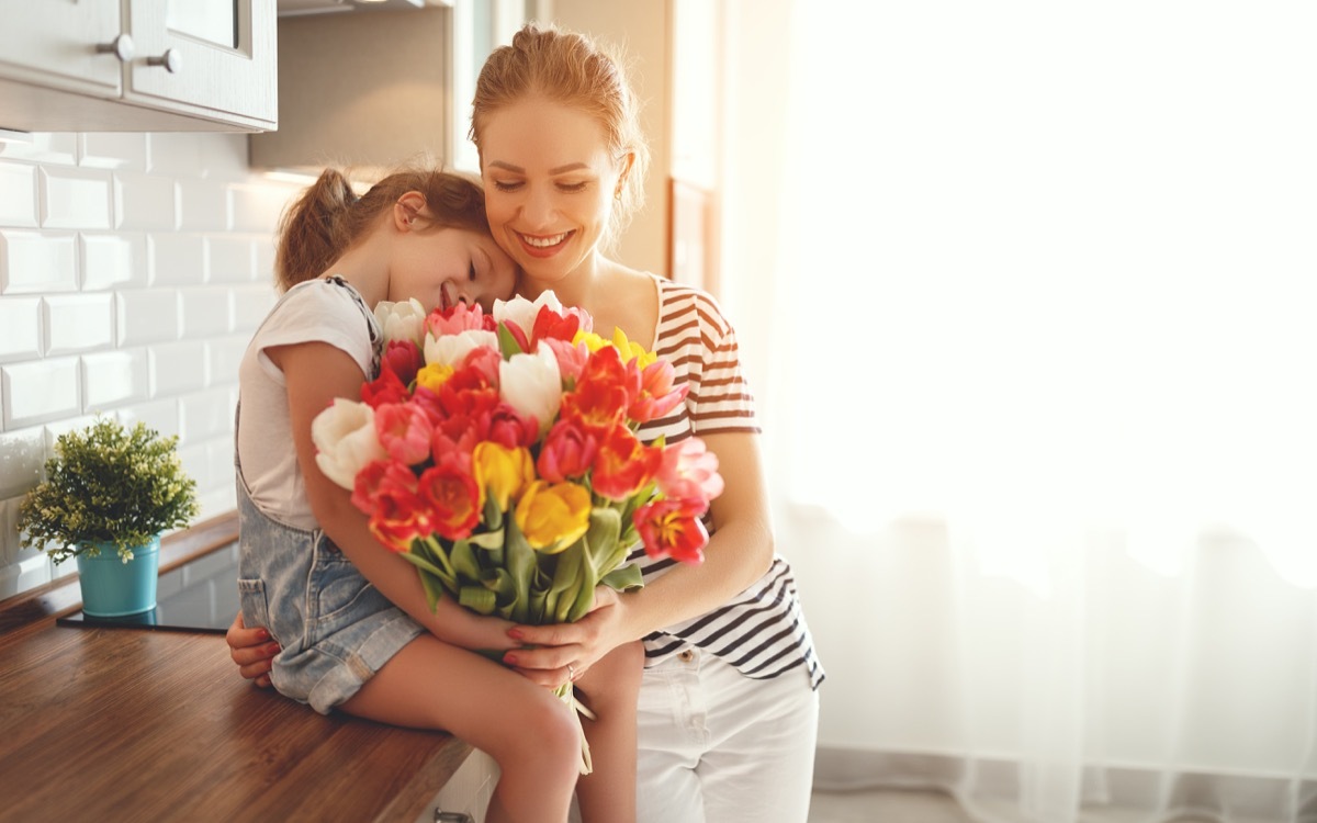 Mother and daughter holding a bouquet of flowers in the kitchen smiling