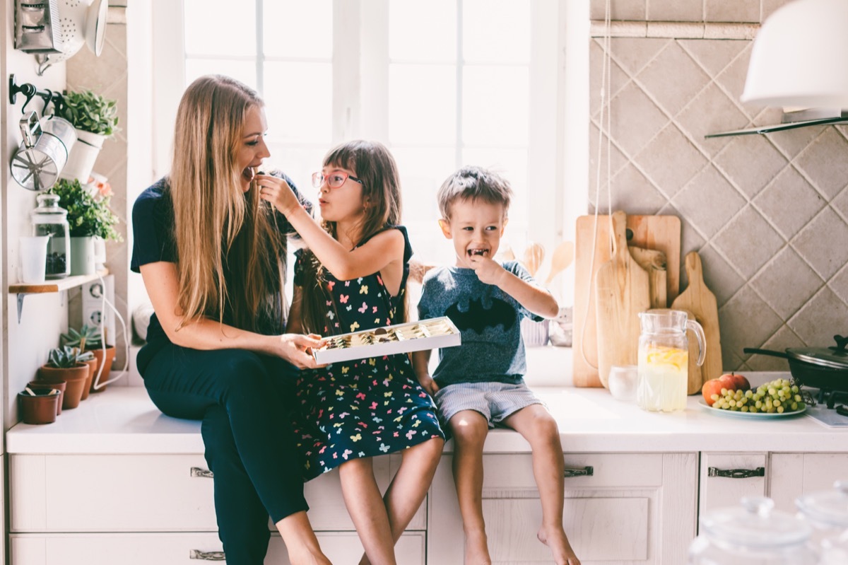 Mom with her two children sitting on the kitchen table and eating candies.