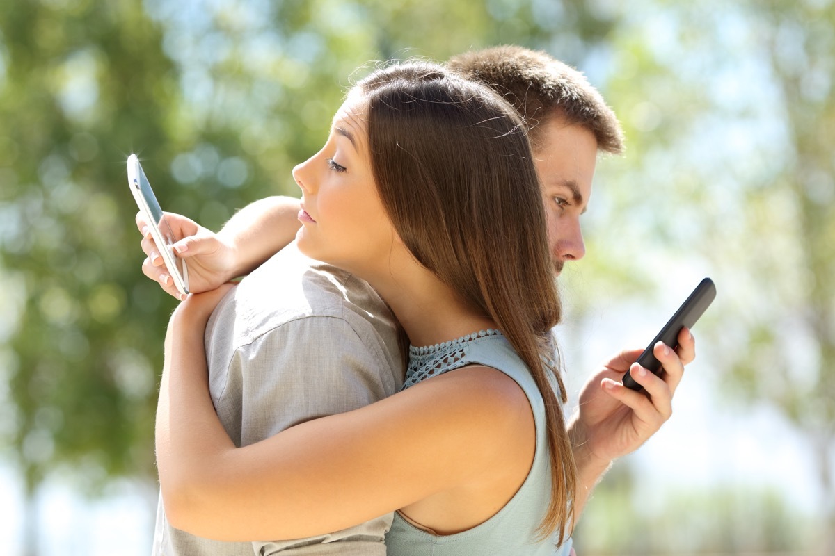 couple cheating on one another uses their cell phones while hugging