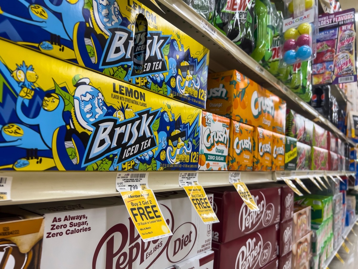 Angled view of various 12 packs of beverages for sale in the soda aisle of a Safeway grocery store.