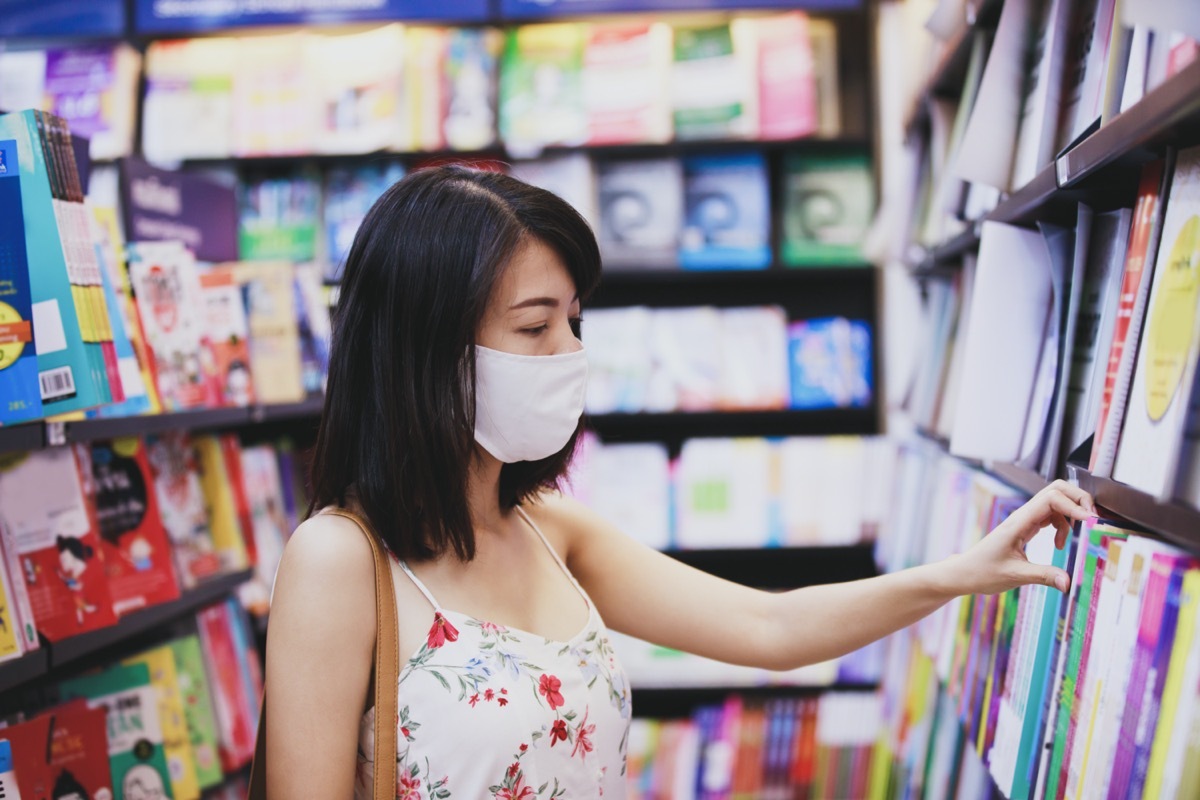 woman wearing face mask choosing book magazine in book store.