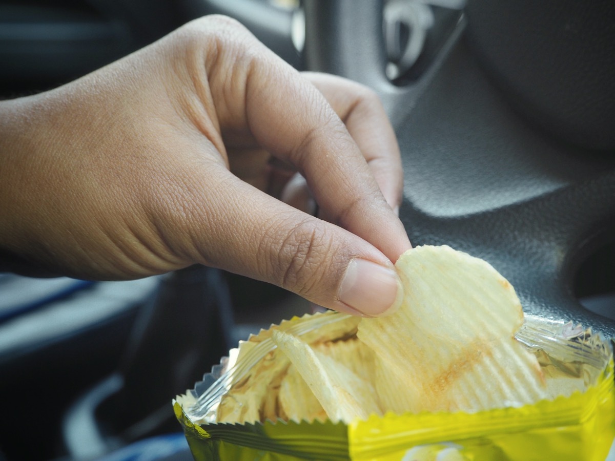 Woman eating potato chip with car