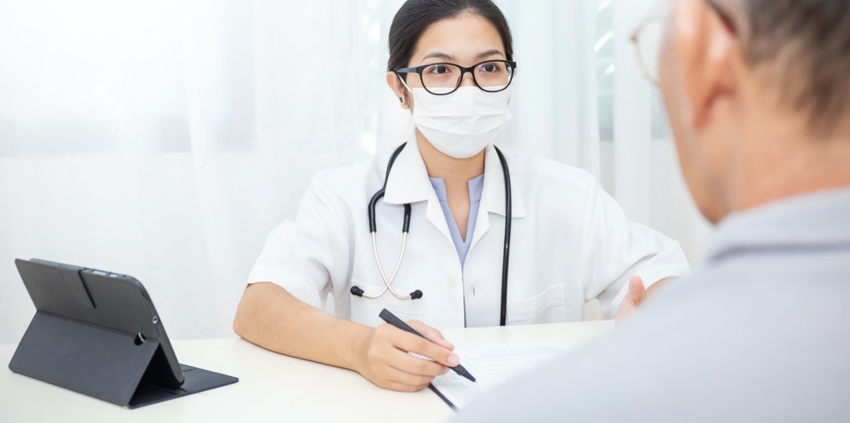 young female doctor wearing glasses and surgical mask talking to older male patient