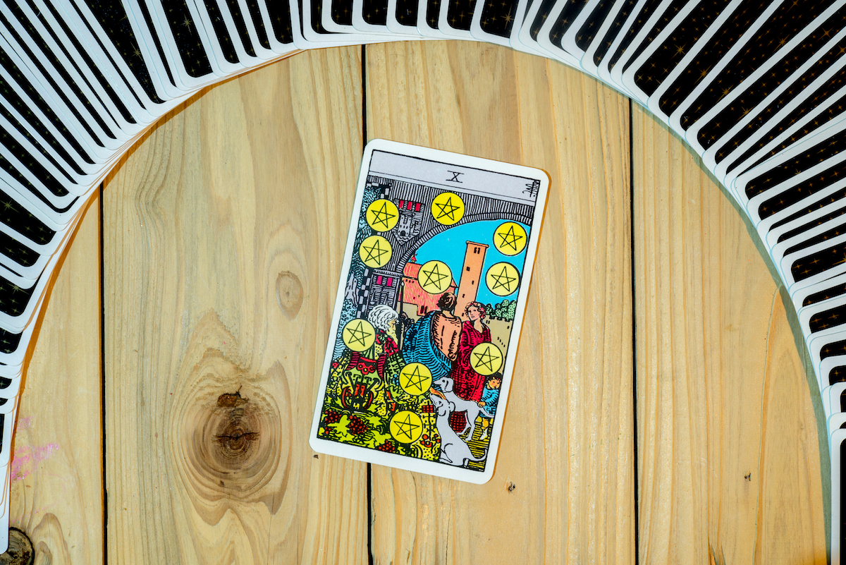 Ten of Pentacles tarot card on wood background with other cards fanned out behind it