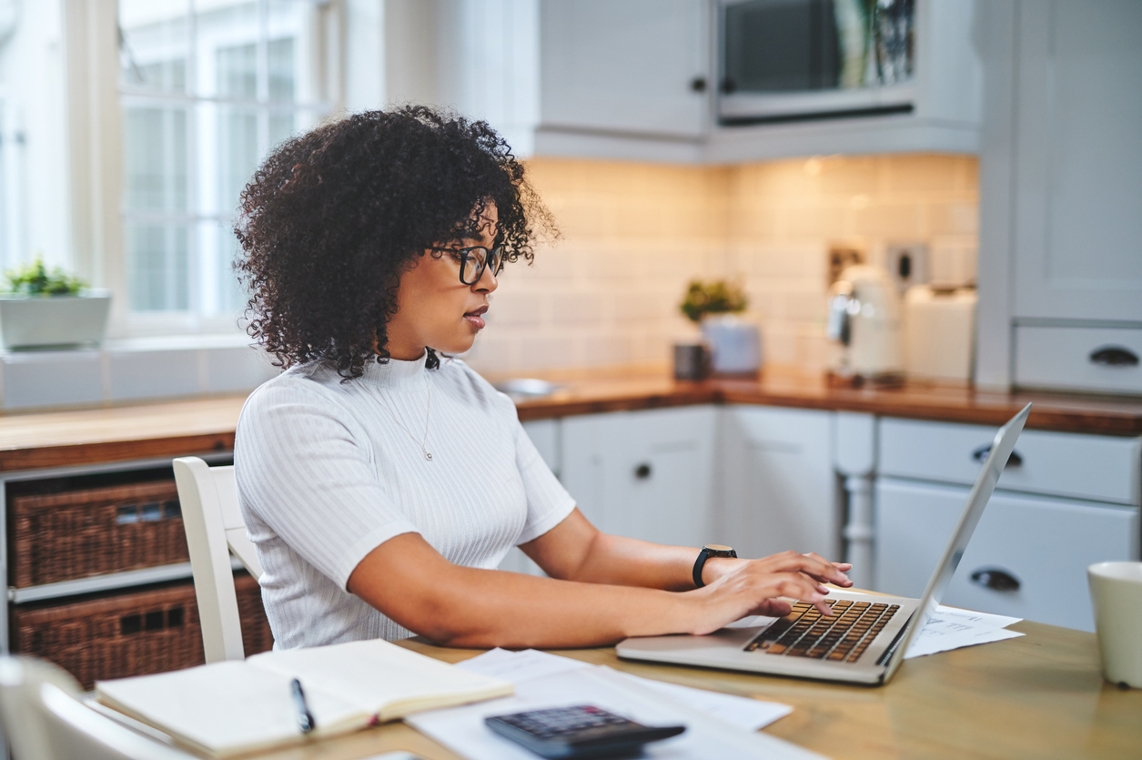 A woman filing her taxes or working from home in her kitchen using a laptop