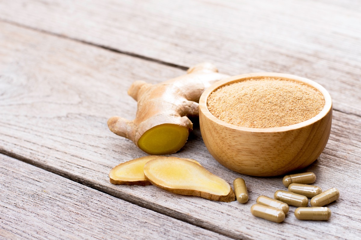 Fresh ginger slice and powder capsules with ginger ground in wooden bowl isolated on wood table background. 
