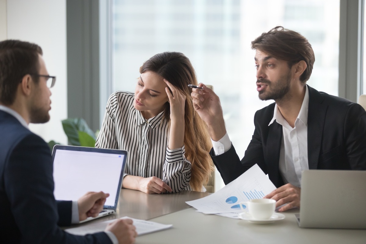 Man interrupting woman talking in business meeting with colleague 