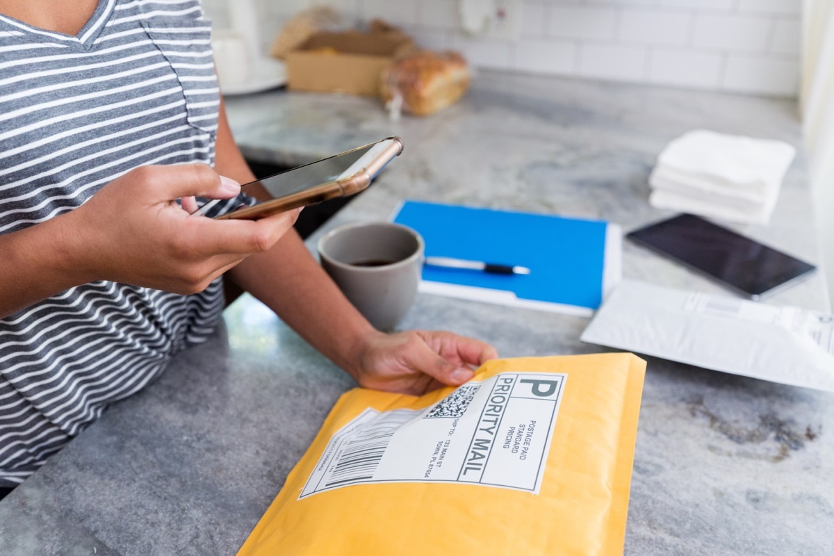 An unrecognizable woman uses a mobile app on her smart phone to prepare a package for mailing.