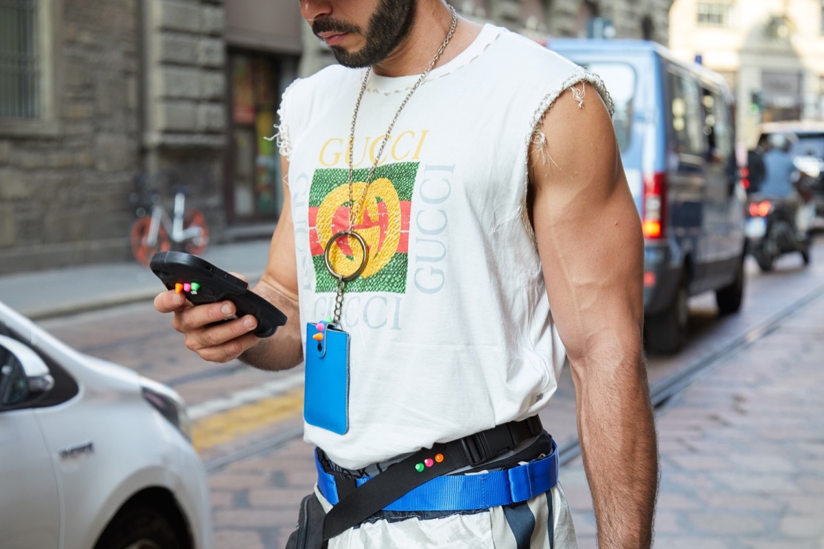 MILAN, ITALY - SEPTEMBER 20, 2018: Man with torn Gucci shirt looking at smartphone before Vivetta fashion show, Milan Fashion Week street style
