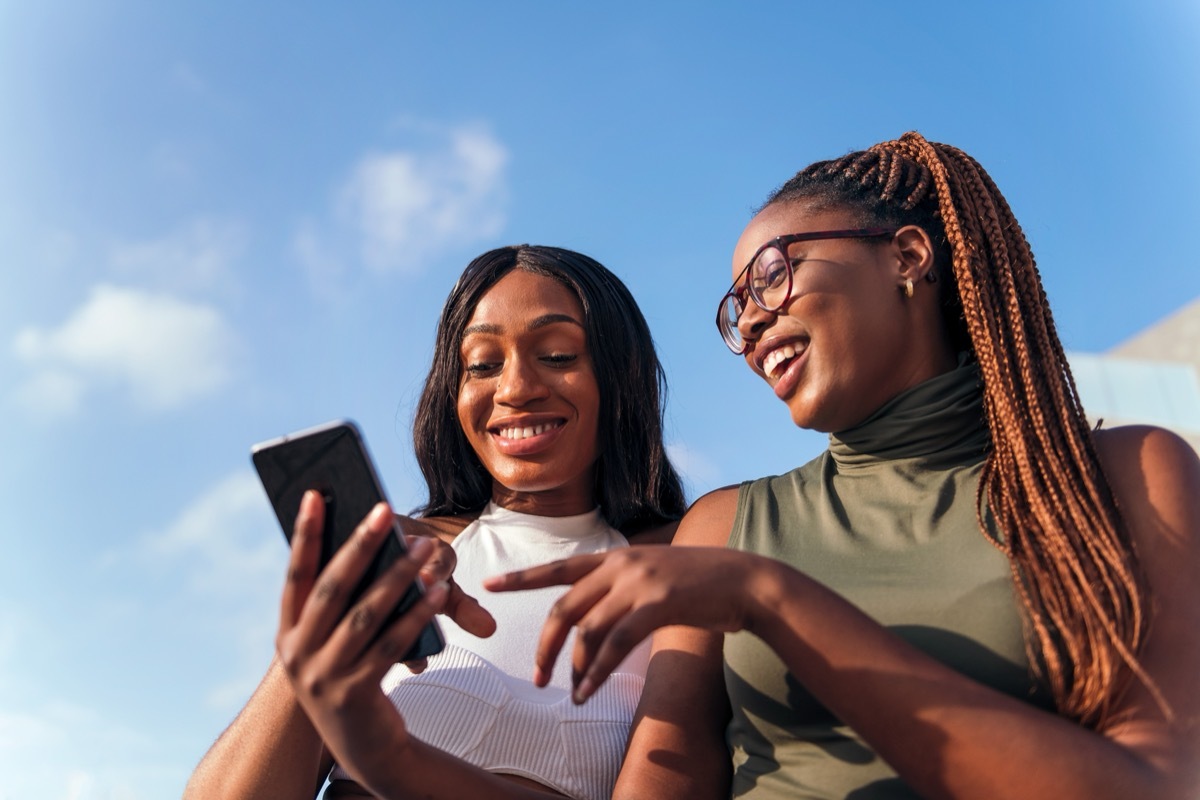 Two young women looking at cell phone while smiling