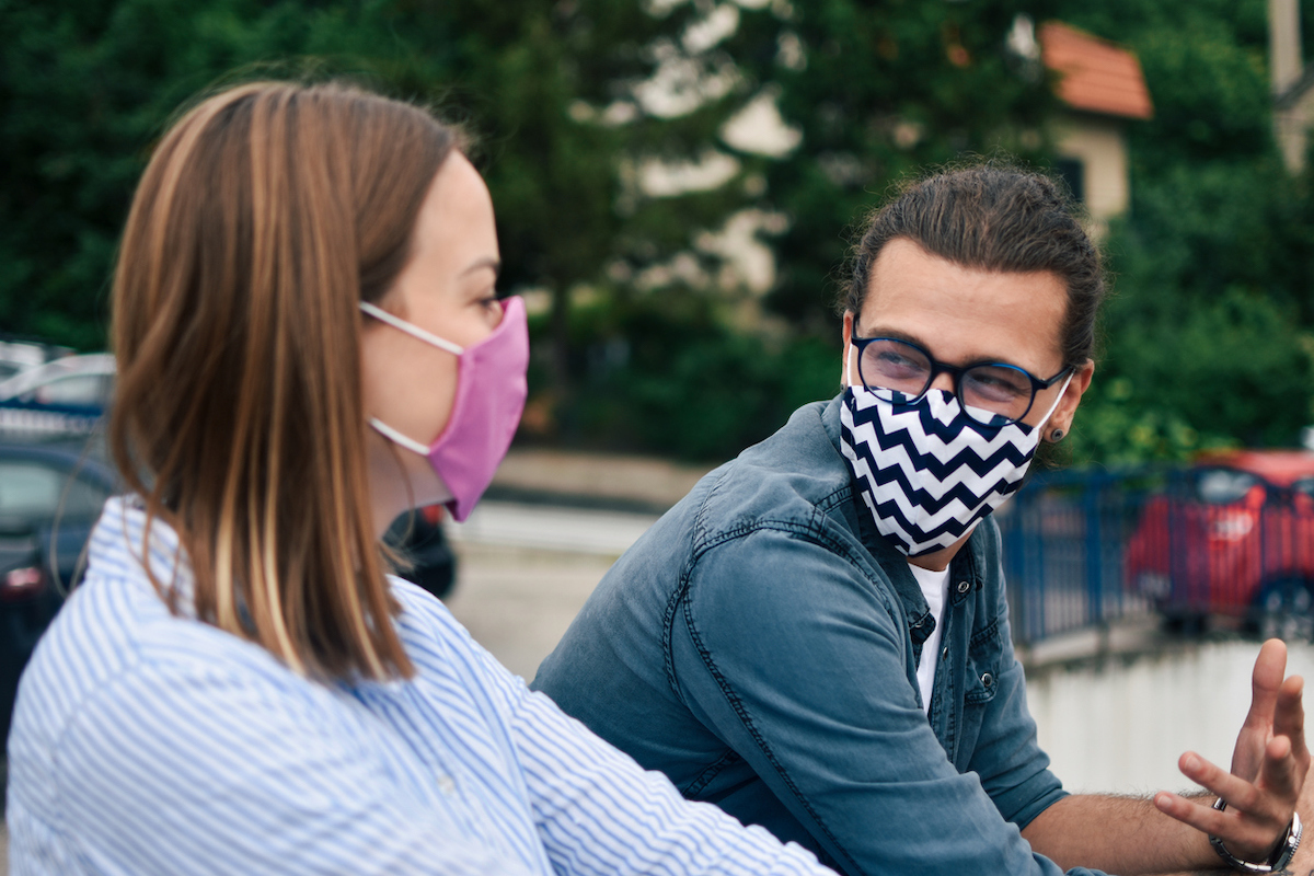 Young man and young woman wearing masks outside and talking