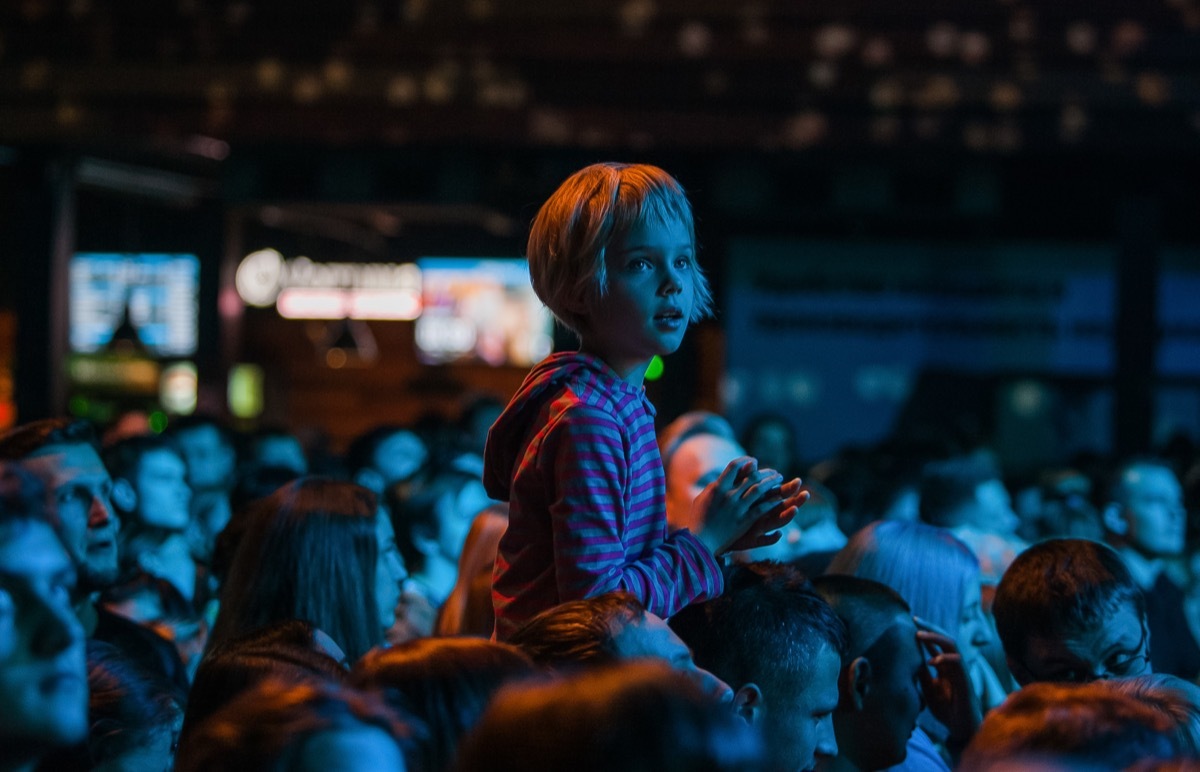 young blonde girl at concert on parent's shoulders