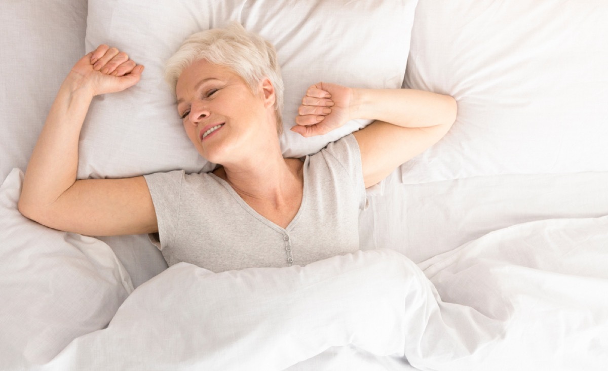 senior white woman stretches in bed as she wakes up