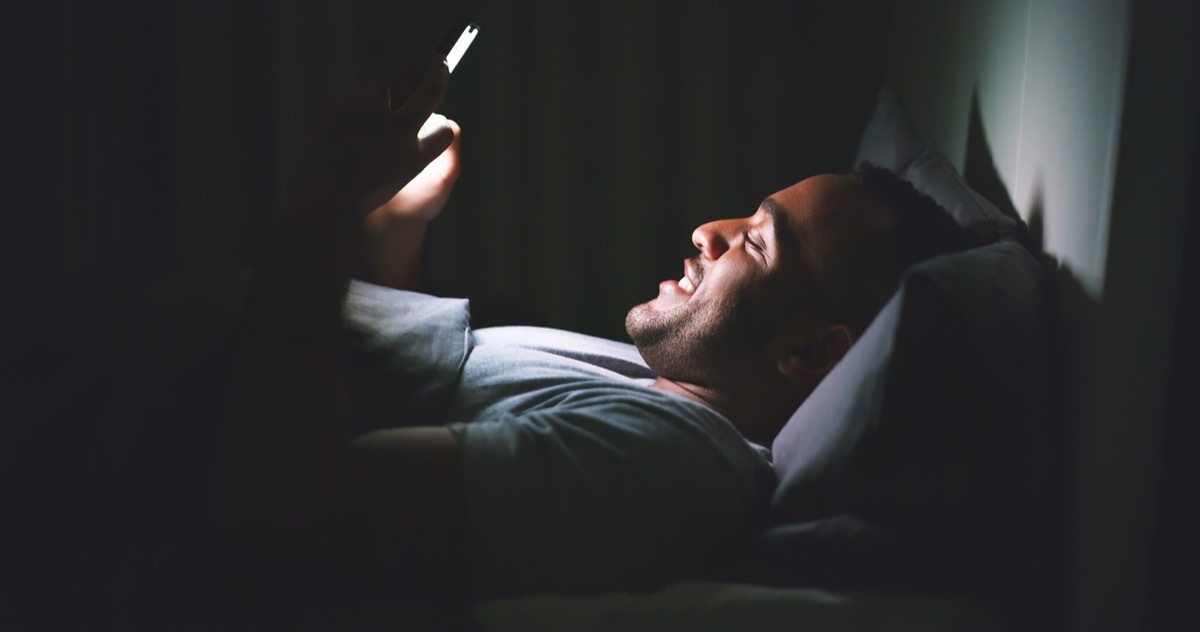 young black man smiling texting late at night in bed