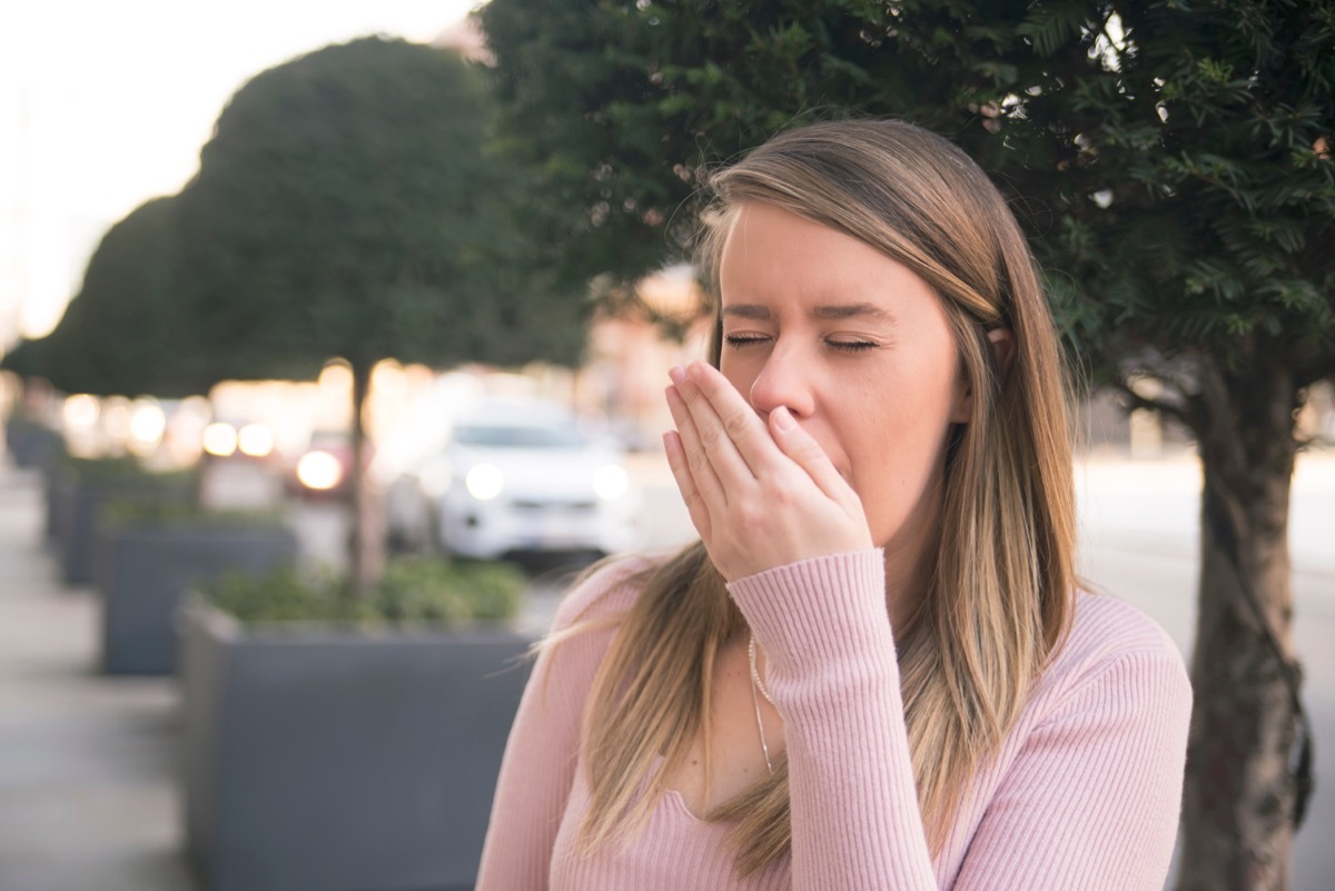 white woman sneezing into hand outdoors