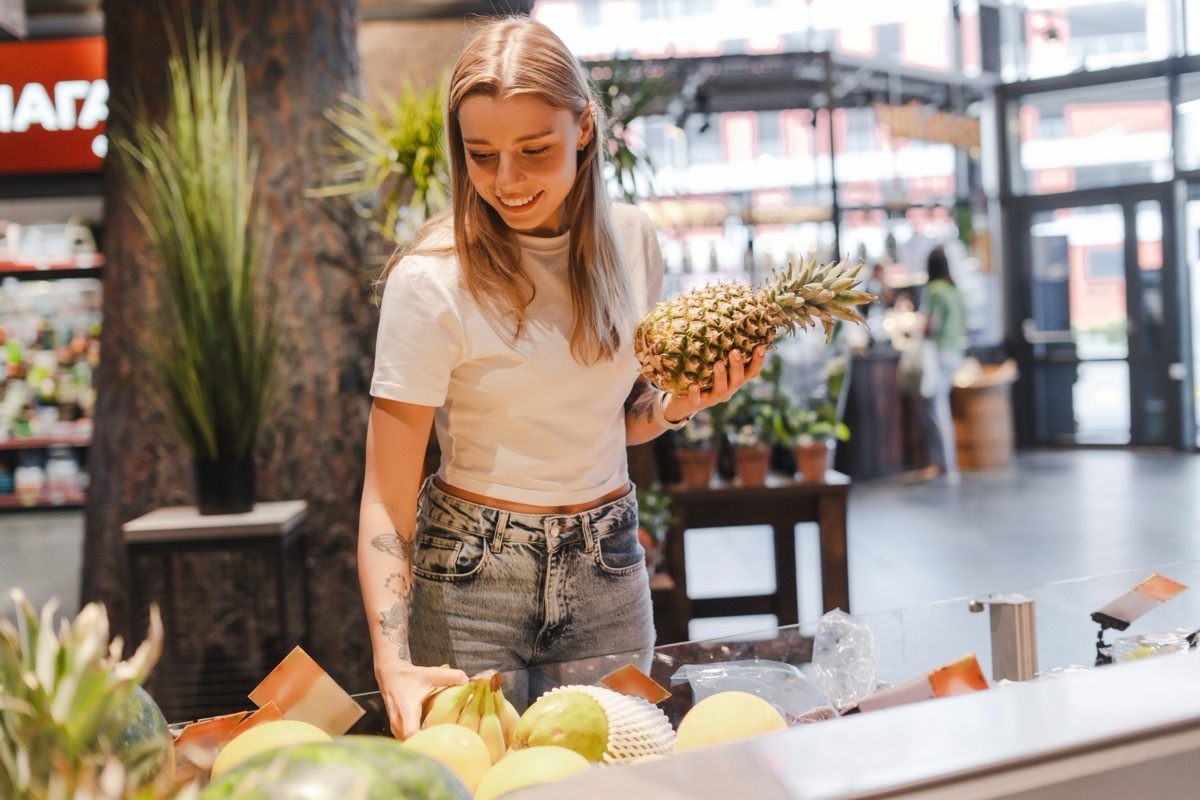 woman holding pineapple at grocery store