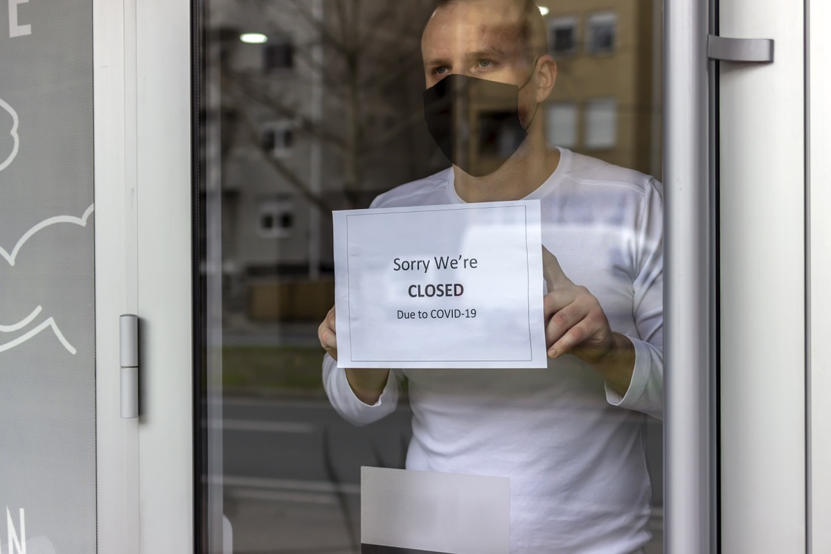Man with protective face mask closing business activity due to covid-19 emergency lockdown quarantine. Man with protective face mask at fitness center entrance holding closing sign due to coronavirus.
