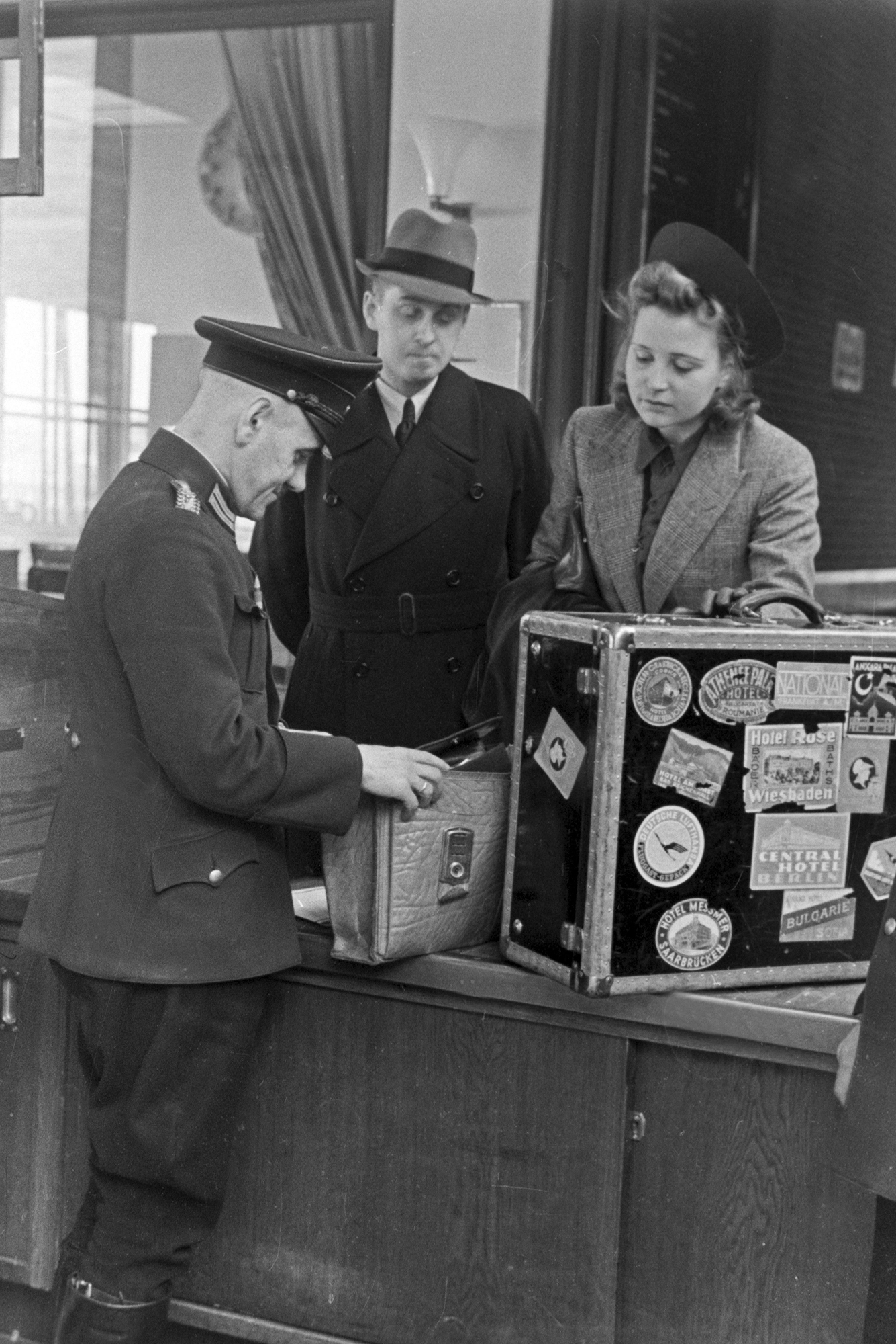 a man and woman watch as a customs officer goes through their suitcases