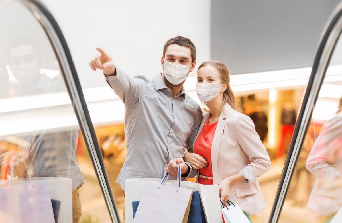 white man and woman wearing face masks going up a mall escalator
