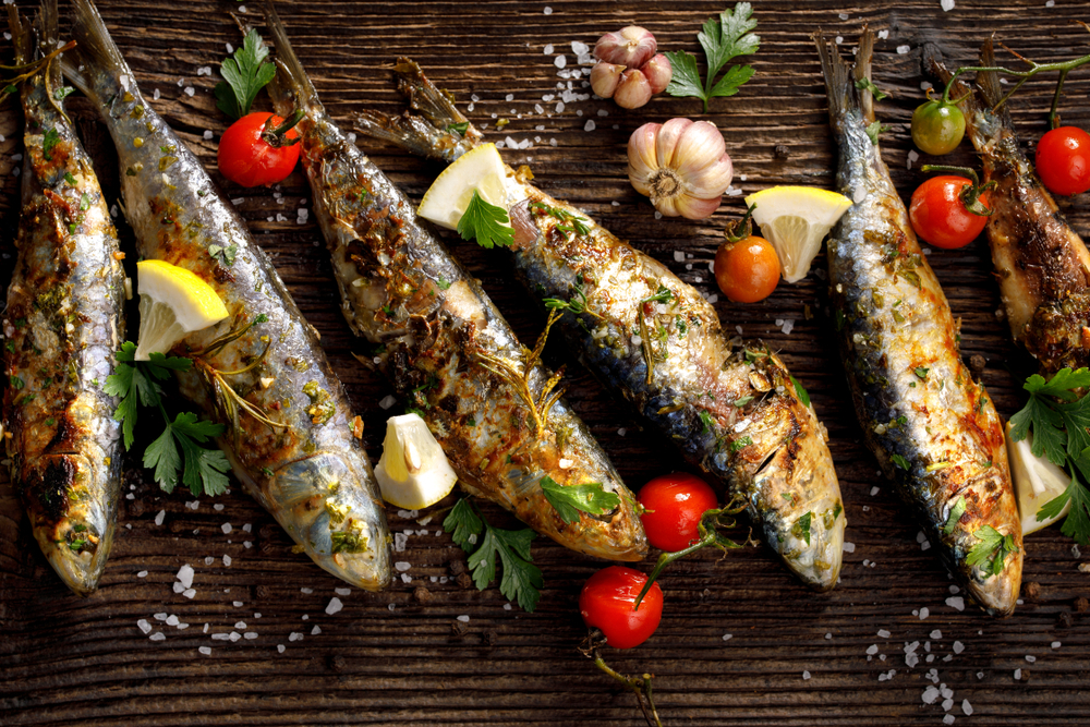 Grilled sardines on a wooden board with tomatoes, lemon, and garlic