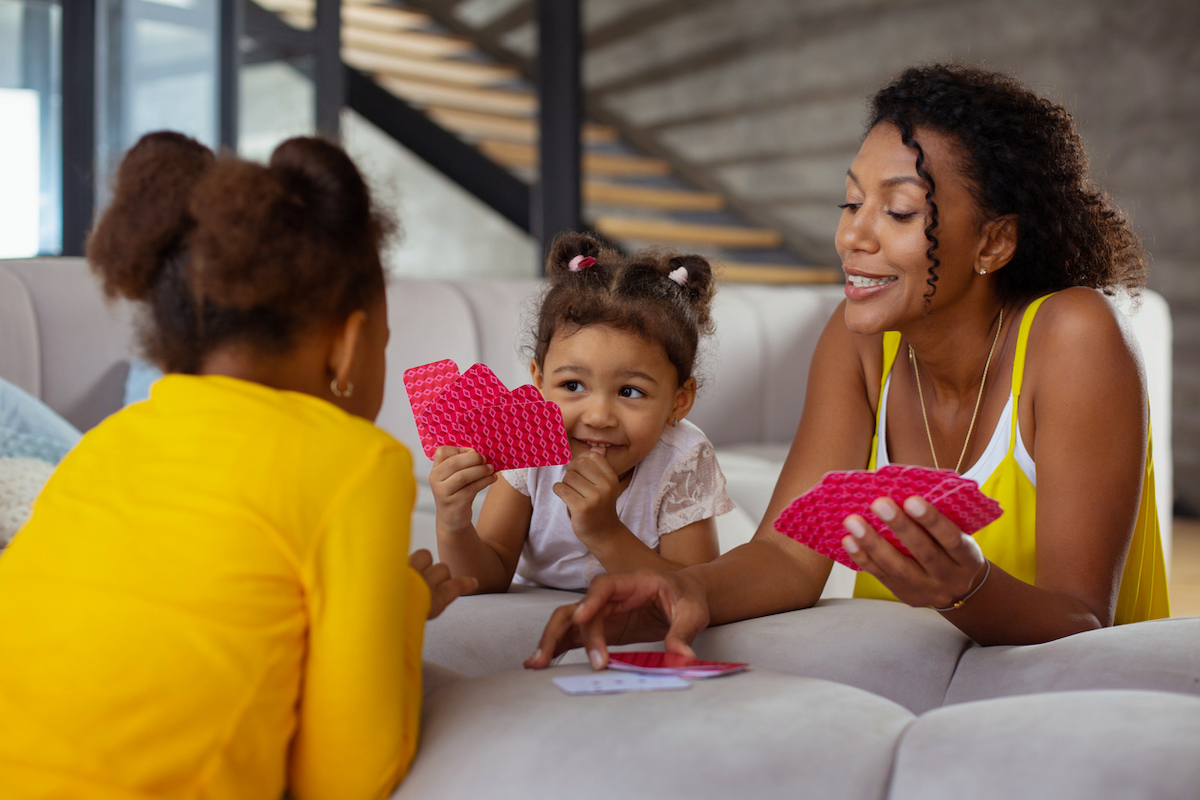 mom playing cards with daughters on couch cushions